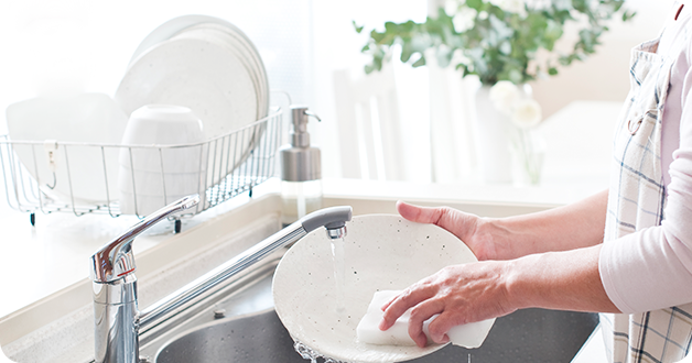 Một người đang rửa tay một cái đĩa trắng trong bồn rửa nhà bếp
